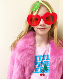 Two red cherries with green rhinestones on a white ballchain necklace with green tassel worn by a girl wearing a pink fur coat and cherry sunglasses