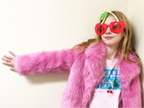 Two red cherries with green rhinestones on a white ballchain necklace with green tassel worn by a girl in a pink fur jacket and cherry sunglasses 